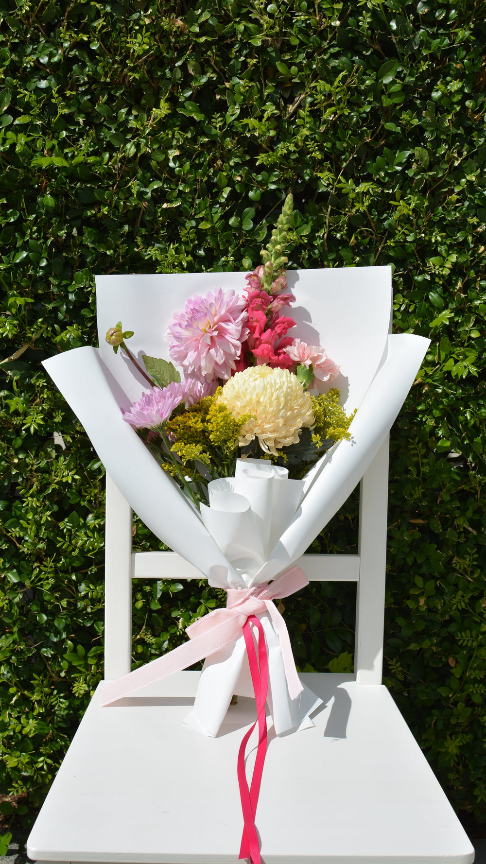 Colourful flower bouquet on a white wooden chair with a green bush backdrop