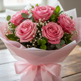 Bouquet of pink roses wrapped in pink paper with a bow on a wooden surface.